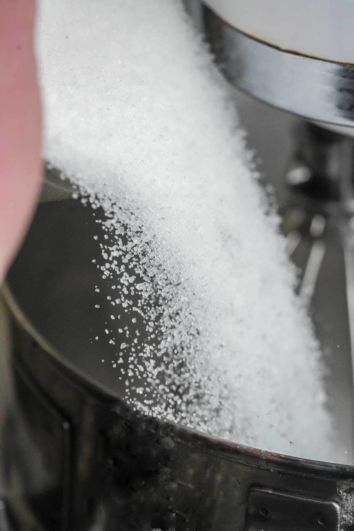 A person pouring sugar into a mixer.
