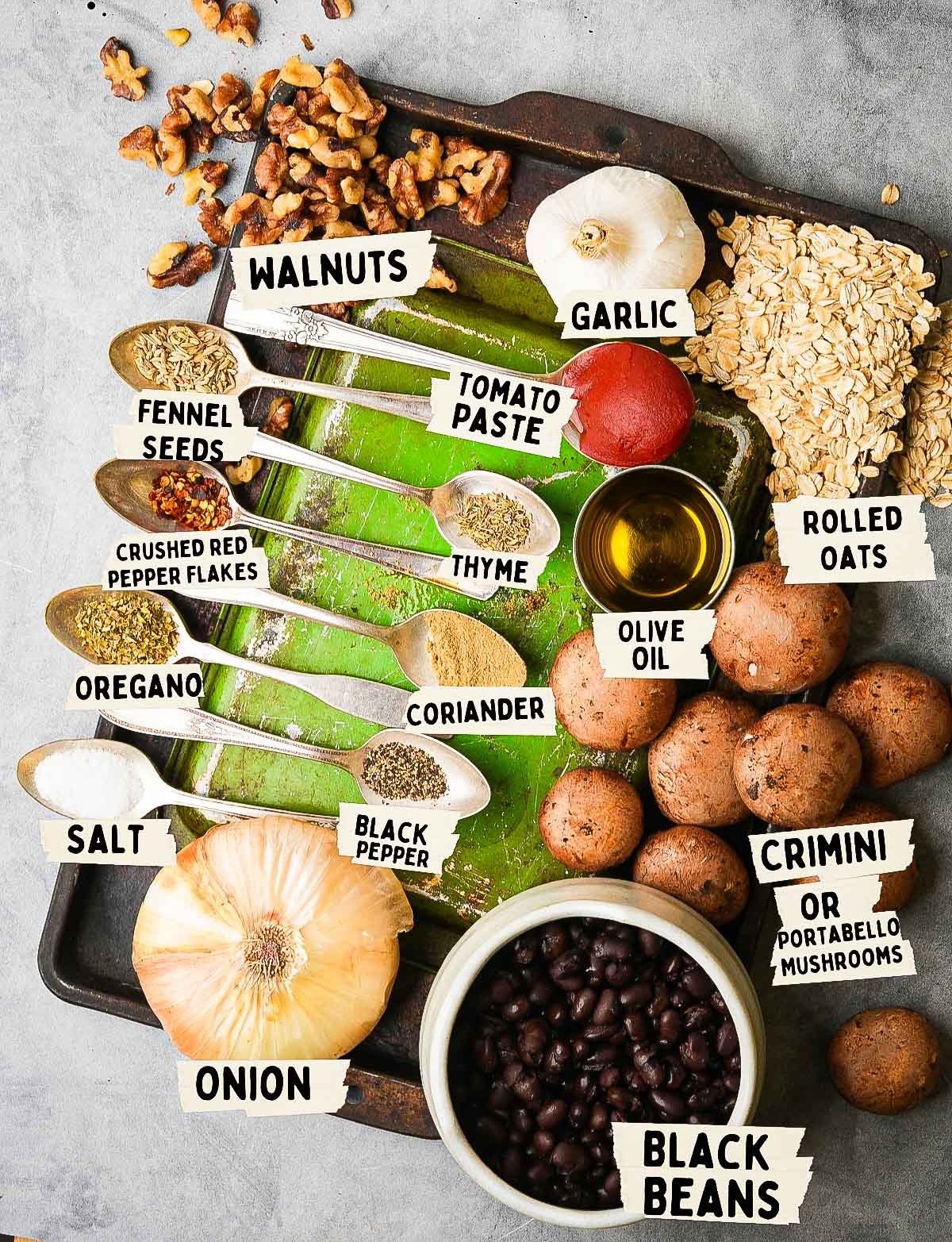 Ingredients for vegan meatballs on a tray: walnuts, garlic, oats, mushrooms, black beans, onion, spices (fennel seeds, oregano, coriander, black pepper, salt, thyme), tomato paste, and olive oil.