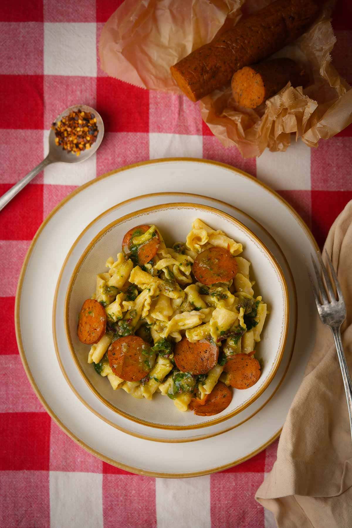 A plate of pasta with vegan pepperoni on a red and white checkered tablecloth.