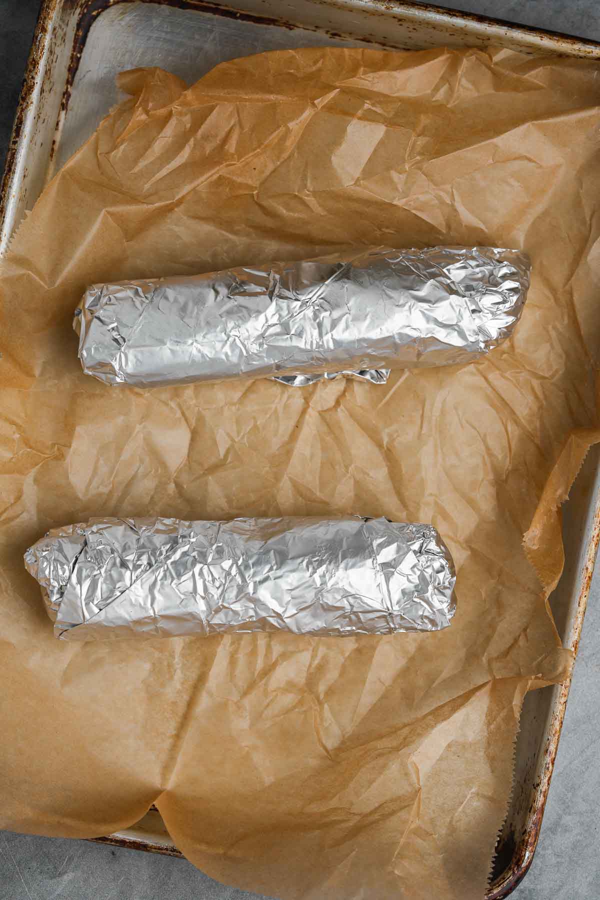 Two foil-wrapped portions of vegan pepperoni dough on a baking sheet.