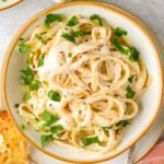 A bowl of creamy vegan fettuccine alfredo pasta garnished with parsley, served with a slice of garlic bread.