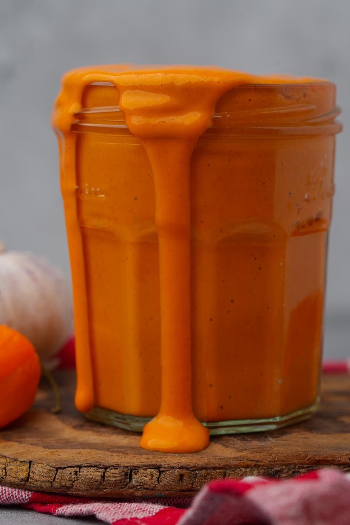 Homemade Vegan Buffalo Sauce overflowing from a glass jar on a wooden surface.