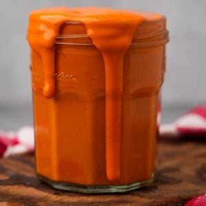 A jar overflowing with thick, creamy Vegan Buffalo Sauce on a wooden surface.