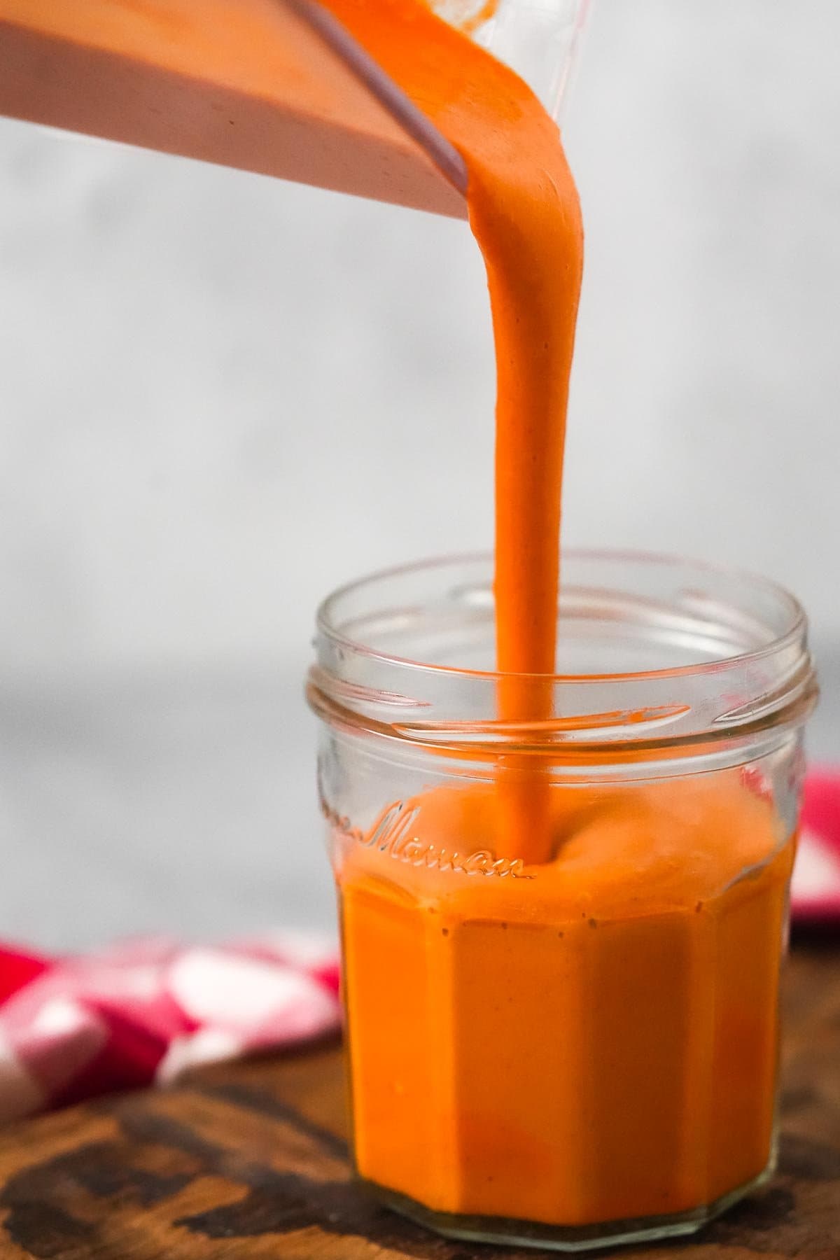 Pouring homemade Vegan Buffalo Sauce into a glass jar.