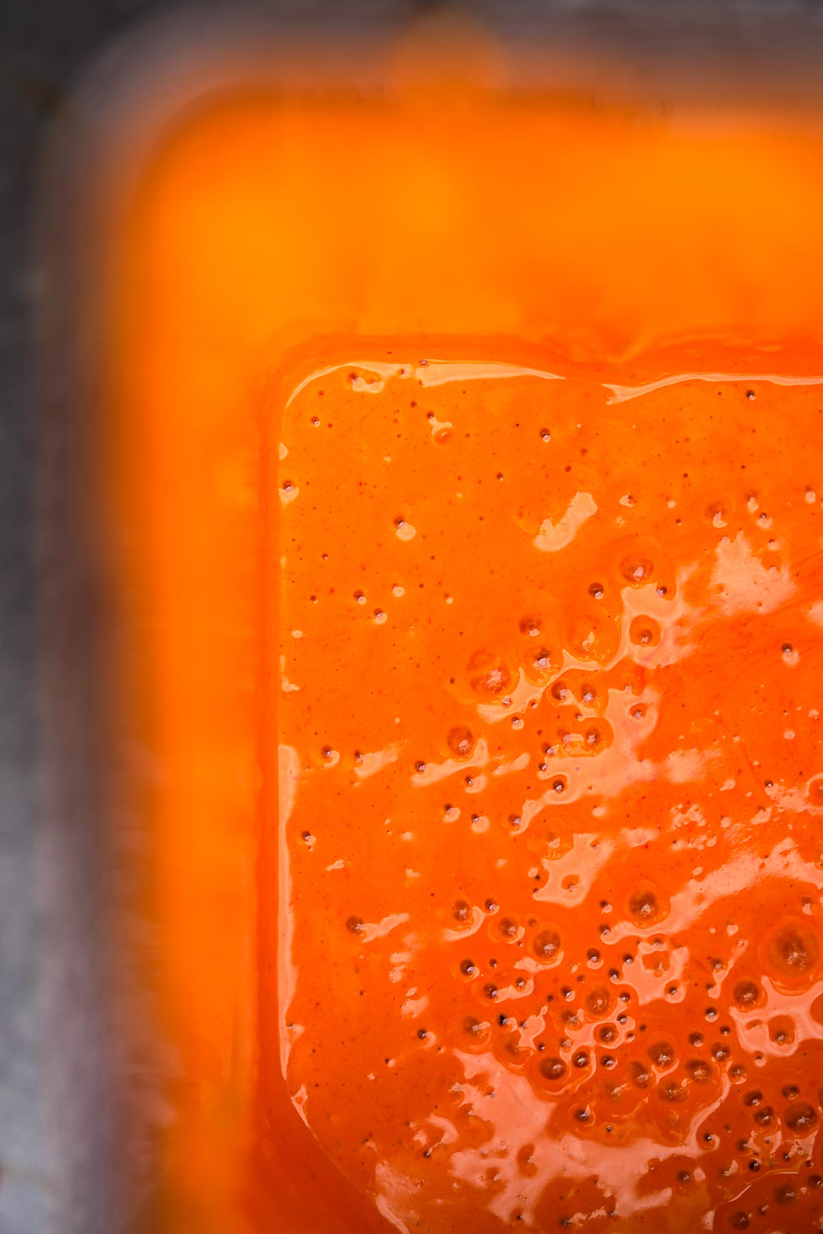 Close-up of a bubbly orange Vegan Buffalo Sauce with a viscous texture.