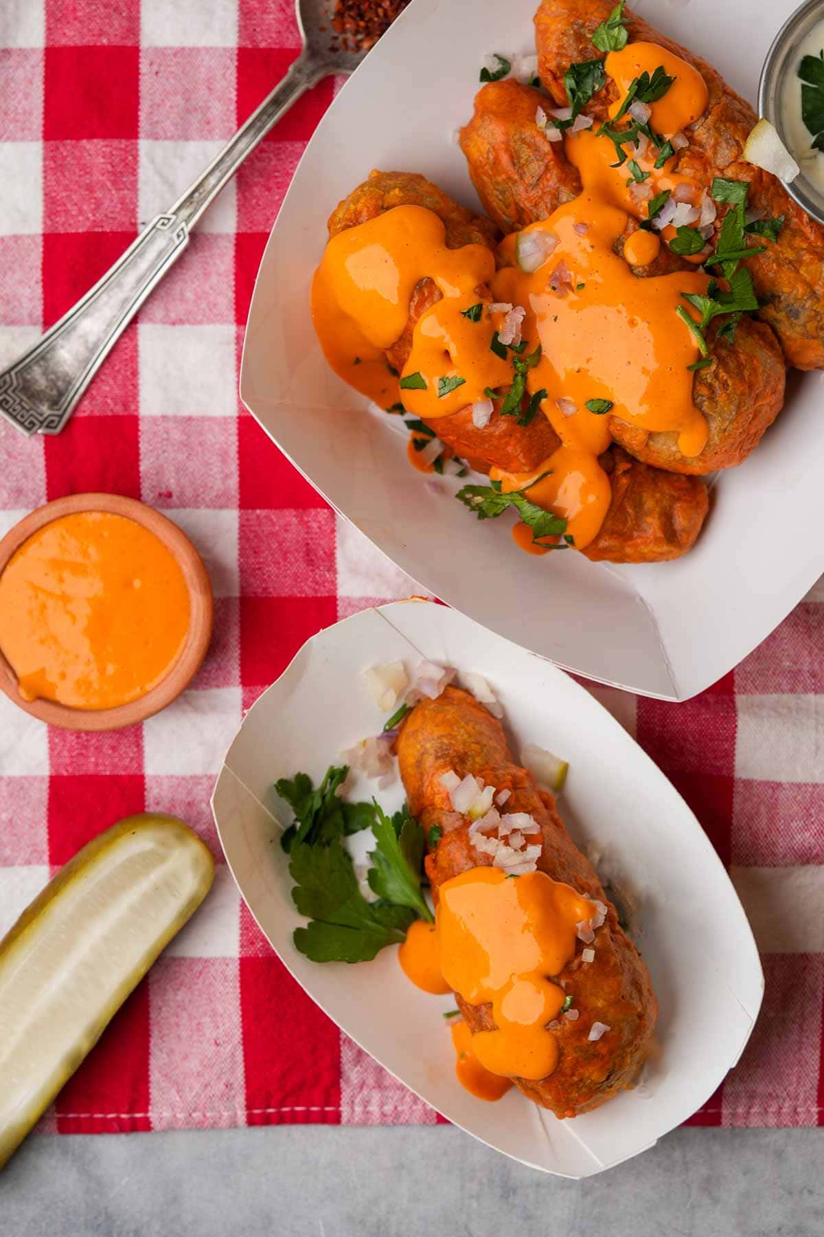 Vegan buffalo wings with creamy orange sauce served on a red and white checkered tablecloth alongside celery sticks and dipping sauce.