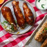 Barbecued vegan drumsticks served with a side of diced onions and a creamy sauce on a ceramic plate.