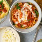 A bowl of fettuccine pasta topped with tomato sauce and a dollop of vegan ricotta cheese, garnished with basil leaves.