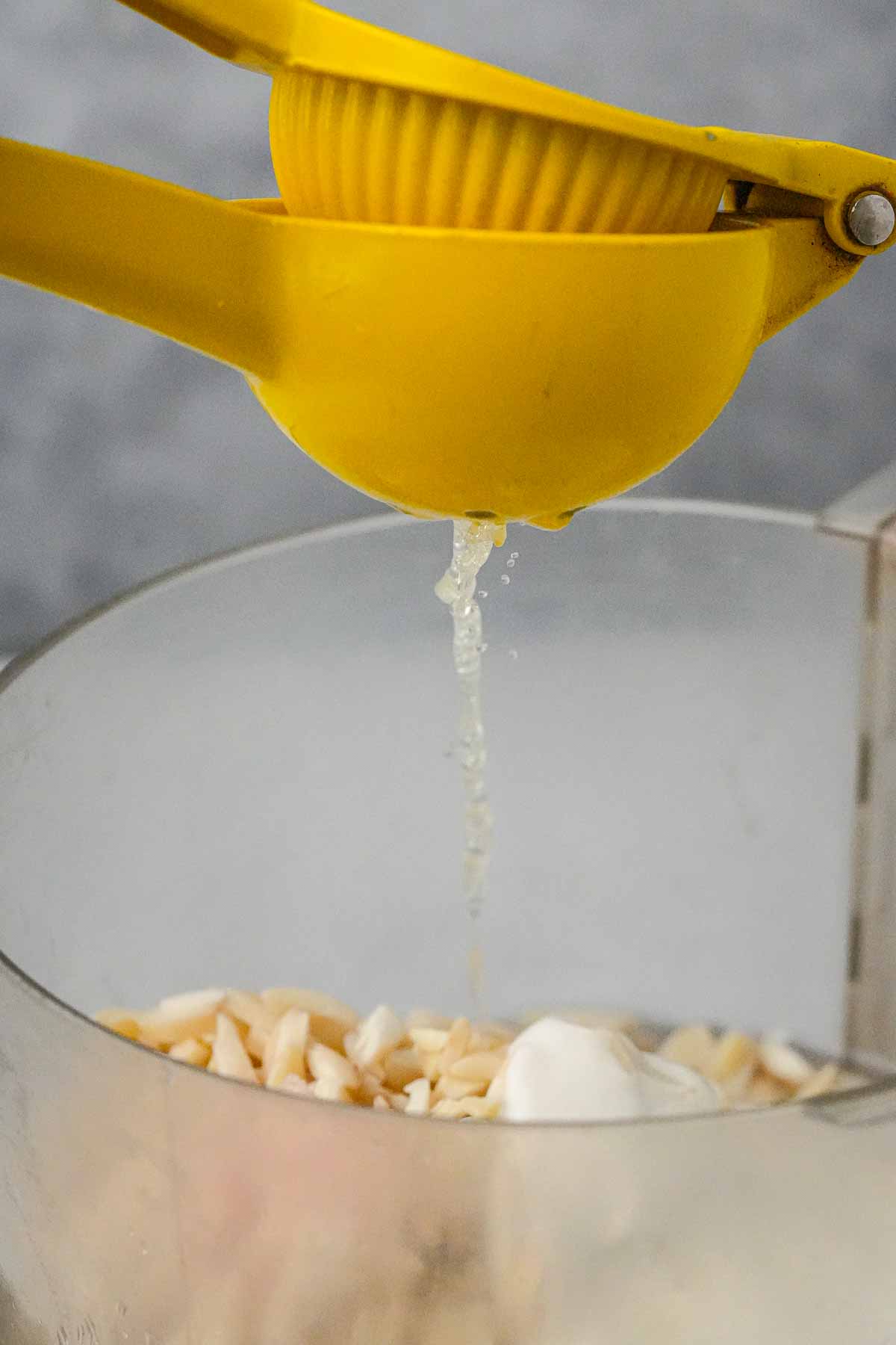 Fresh lemon juice being squeezed into a food processor container with chopped ingredients.