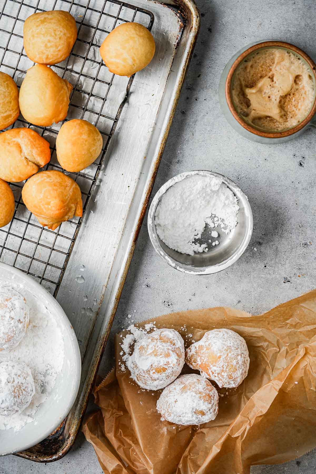 Freshly fried round Zeppole dusted with powdered sugar, displayed on a kitchen countertop with a cup of coffee and additional sugar for serving.