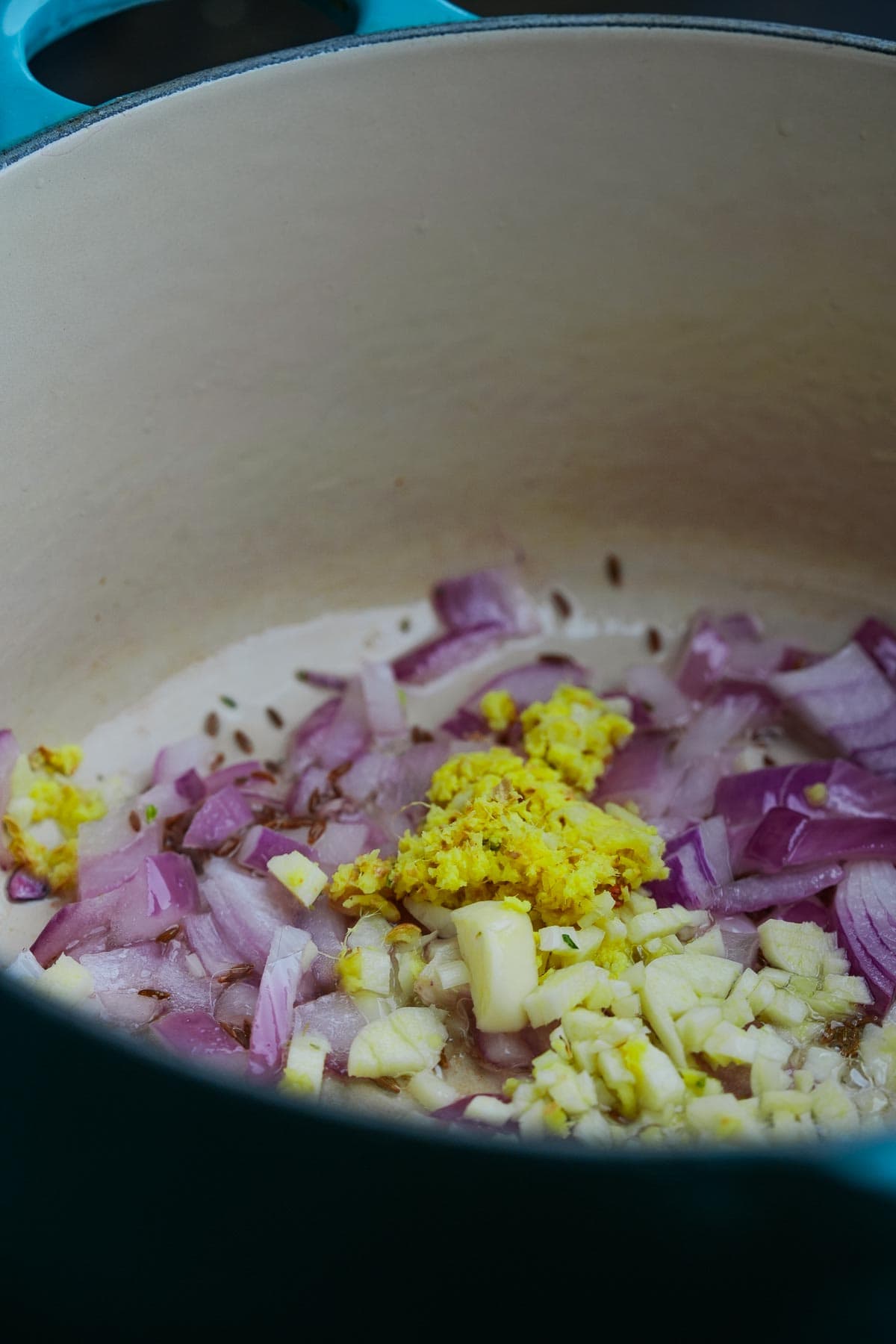 Sautéed red onions, garlic, and ginger in a light-colored pot.