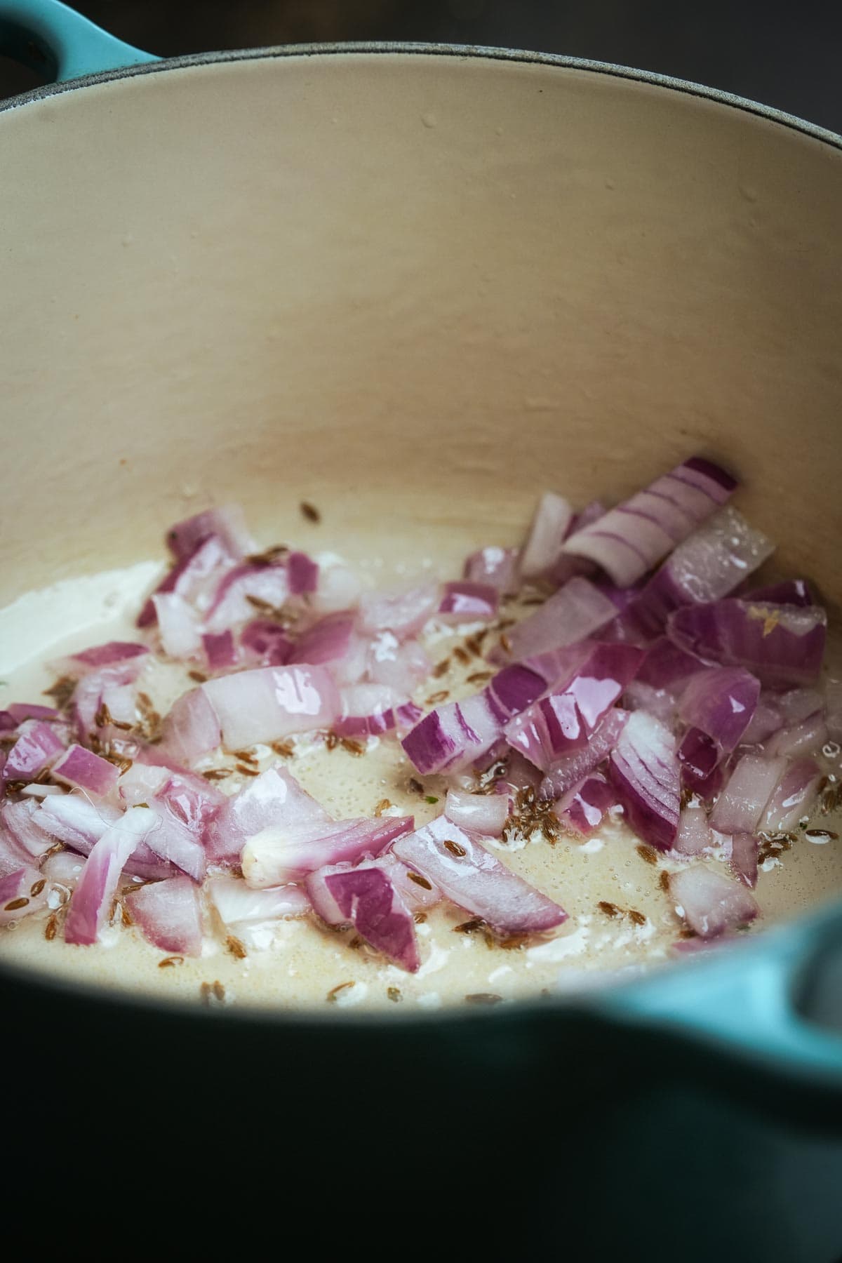 Chopped red onions sautéing in a light-colored pot, with visible spices and oil.
