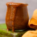 A jar of homemade Tamarind Chutney overflowing, placed on a green ceramic plate.