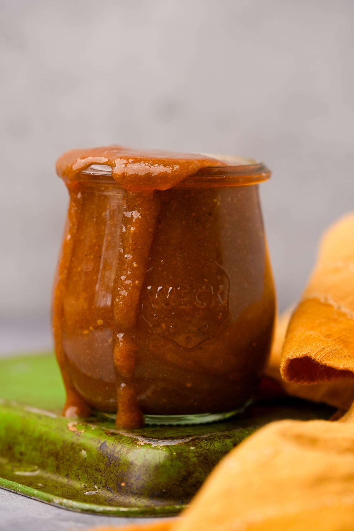 A jar of homemade Tamarind Chutney overflowing, placed on a green ceramic plate.