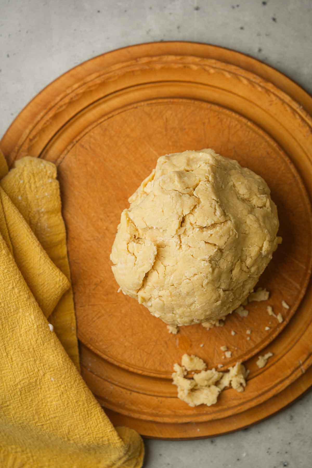 A ball of vegan pie dough on a wooden plate beside a yellow cloth.