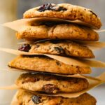 A stack of vegan oatmeal raisin cookies separated by parchment paper.