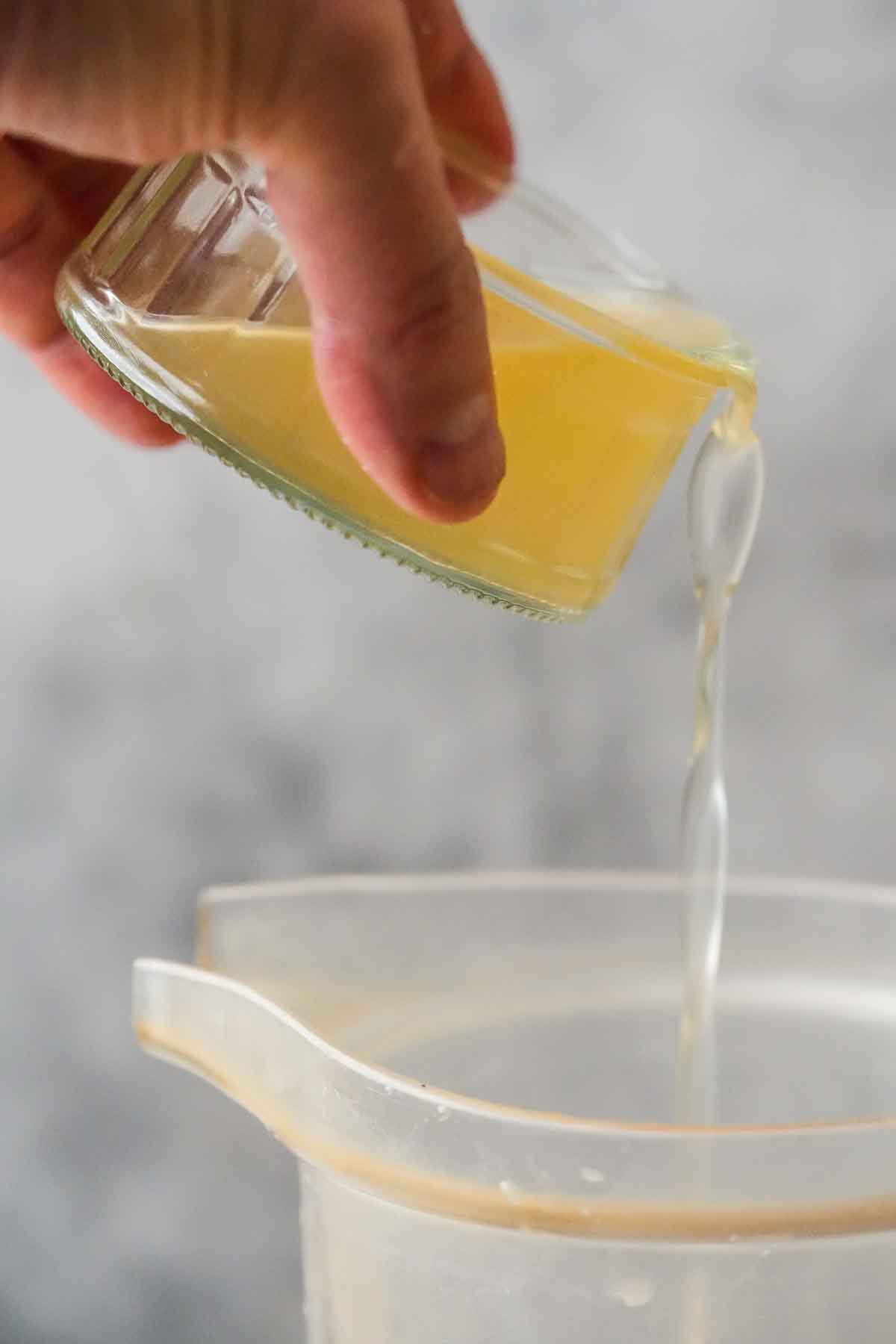 Pouring aquafaba from a glass cup into a blender pitcher.