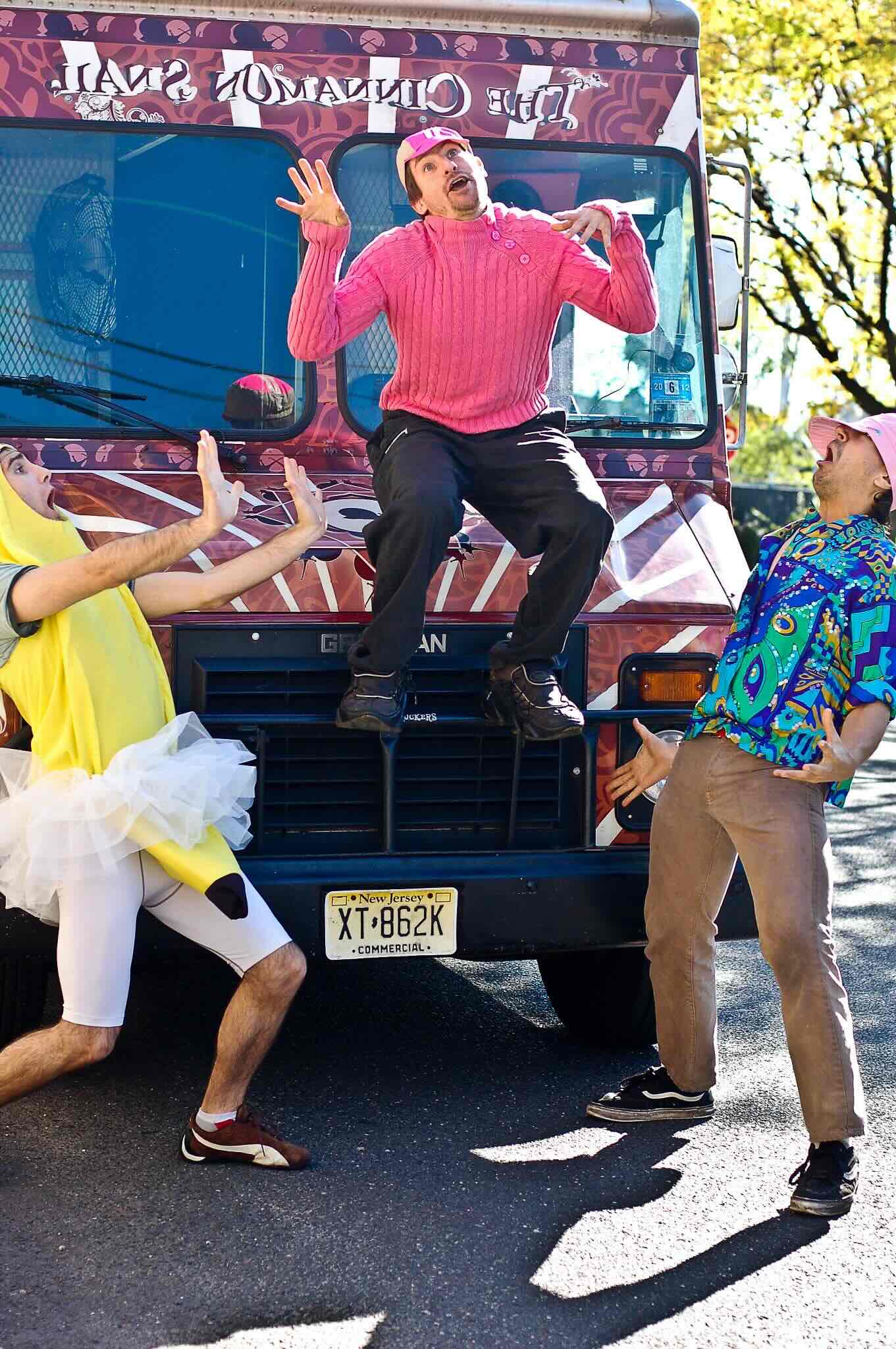 Adam Sobel and two individuals in colorful costumes pose playfully in front of the cinnamon snail food truck.