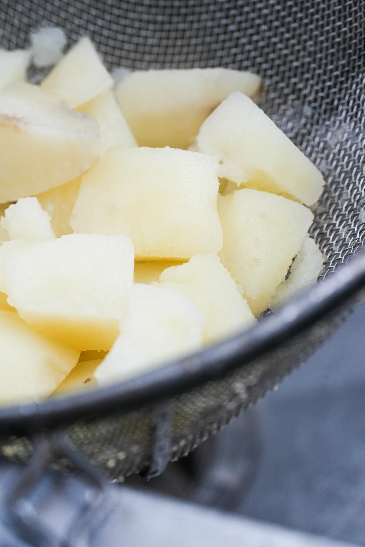 Cooked potatoes cooling in a metal colander.