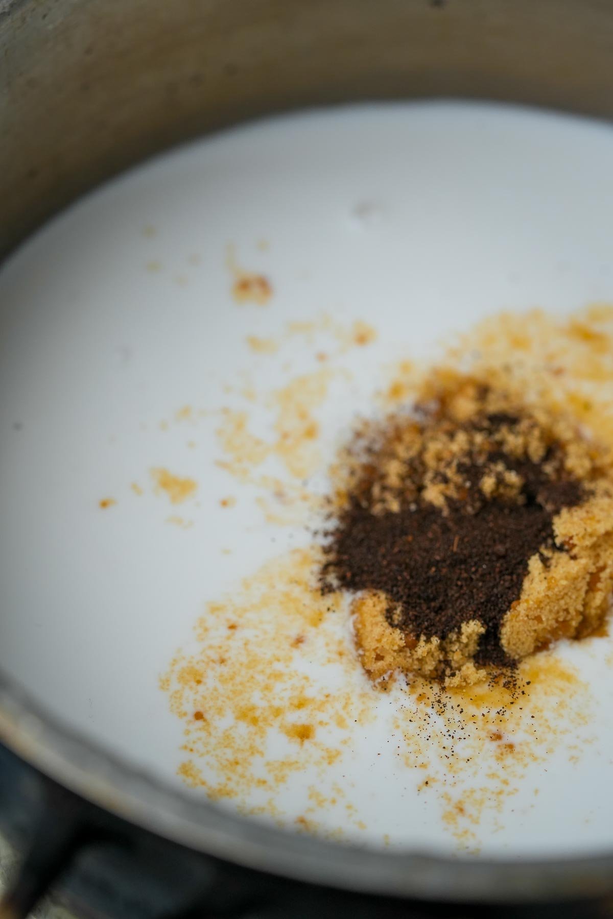 A close-up of white coconut milk in a pot with brown sugar and vanilla powder.