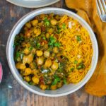 A bowl containing yellow rice and chickpea spinach curry, placed on a wooden surface beside a yellow napkin and a fork.