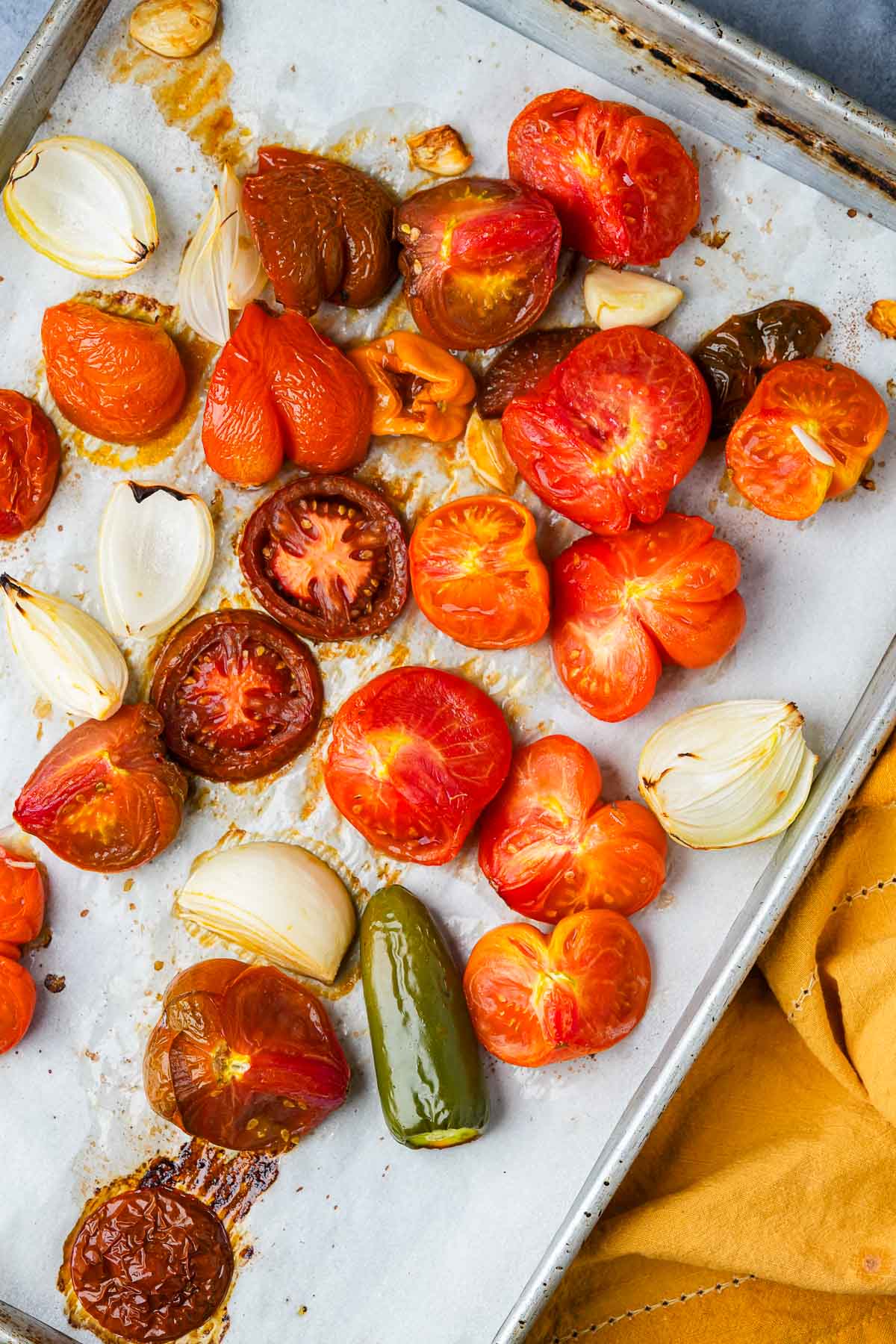 Roasted tomatoes, garlic, and onions on a baking sheet, displaying vibrant colors and caramelization.