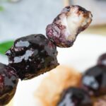 Three dark, glossy Karioka skewers, one of which shows a bite taken out, revealing a white filling inside.