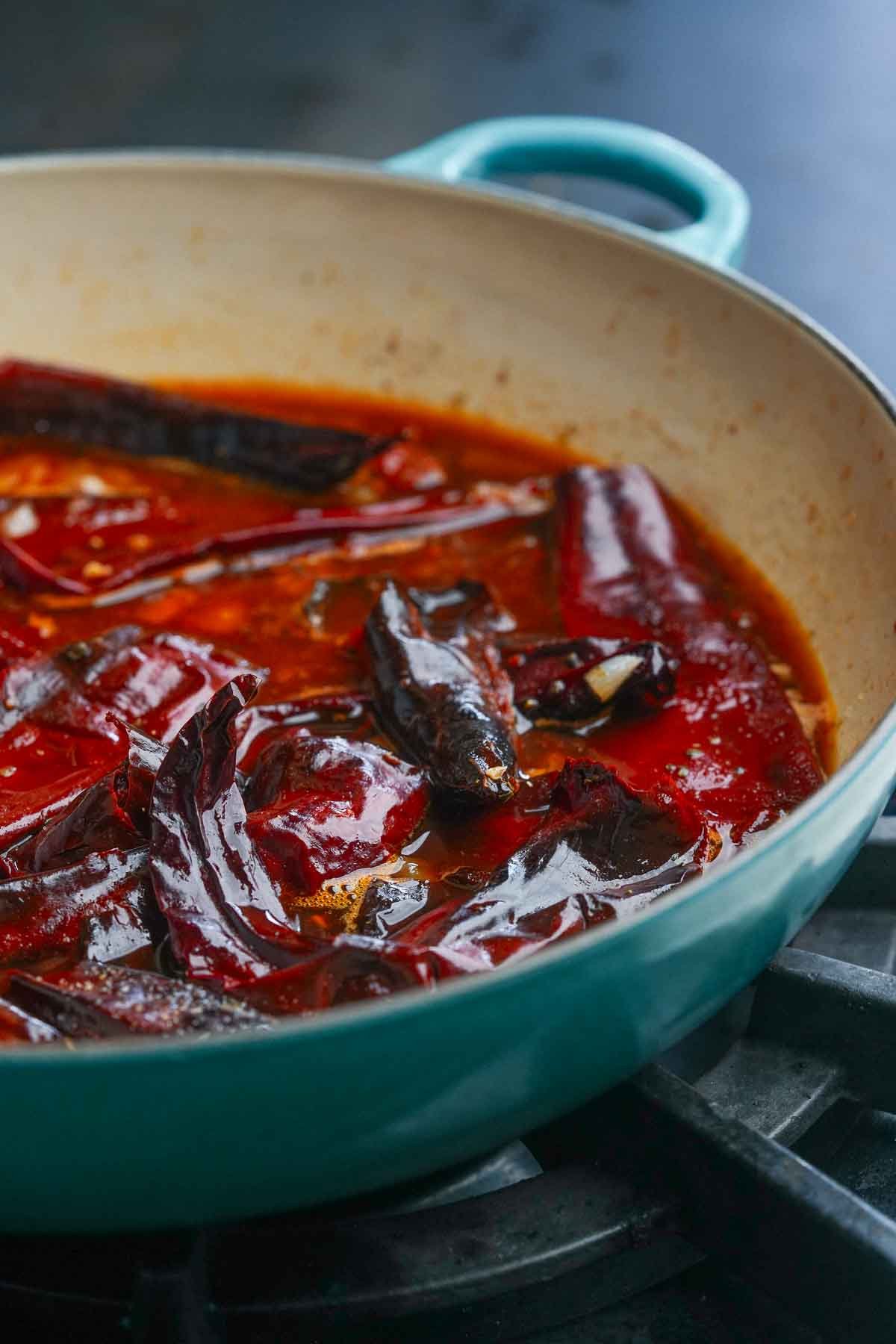 An enamel pan on a stove containing rehydrated dried red chili peppers and other ingredients for making red chili saucew.
