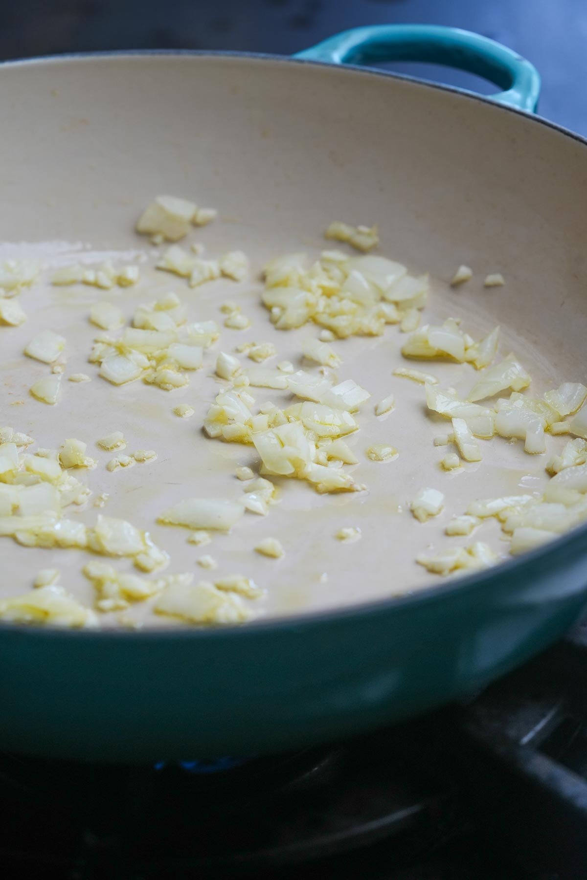 Chopped garlic and minced onion sautéing in oil in a light blue skillet on a stove.