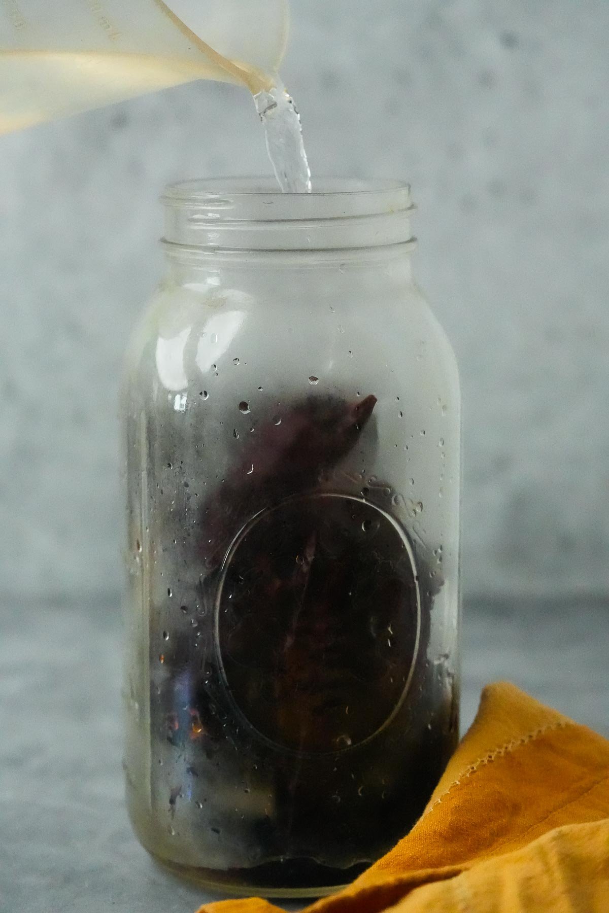 Hot water being poured into a glass jar containing dried hatch chilies.
