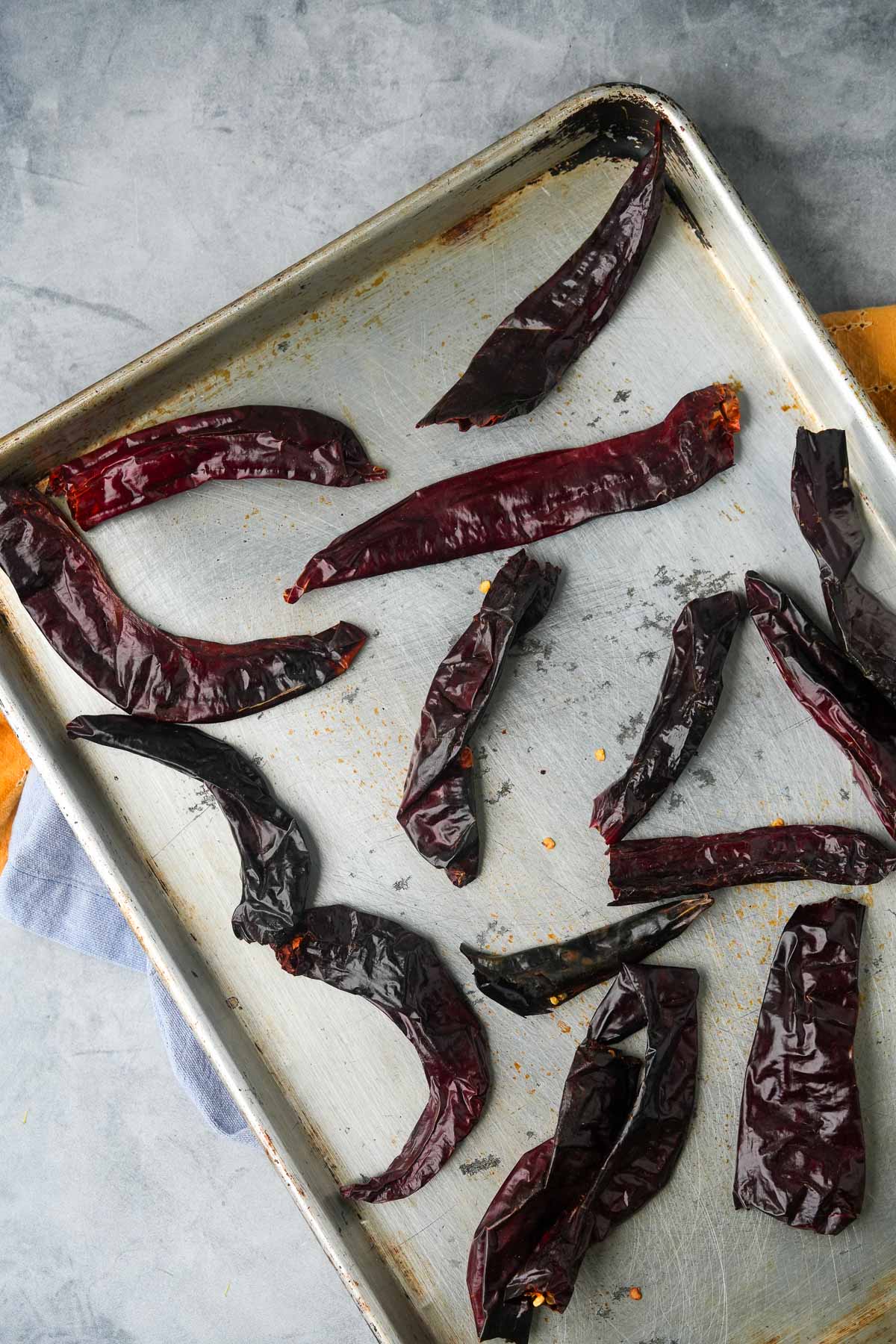 Dried chili peppers arranged on a used baking sheet, showing signs of wear and residual spices.