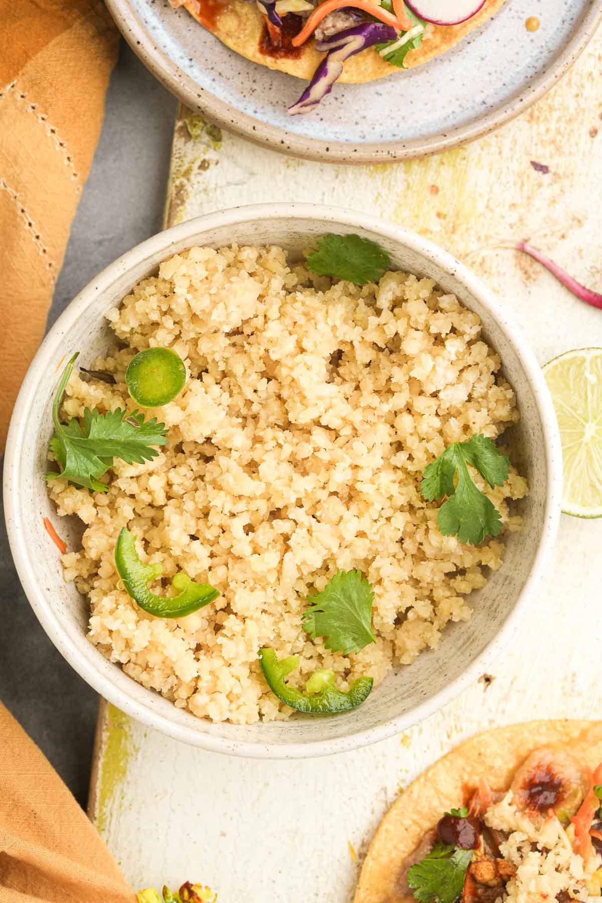 Bowl of Vegan Cotija Cheese garnished with cilantro and jalapeno slices on a textured surface.