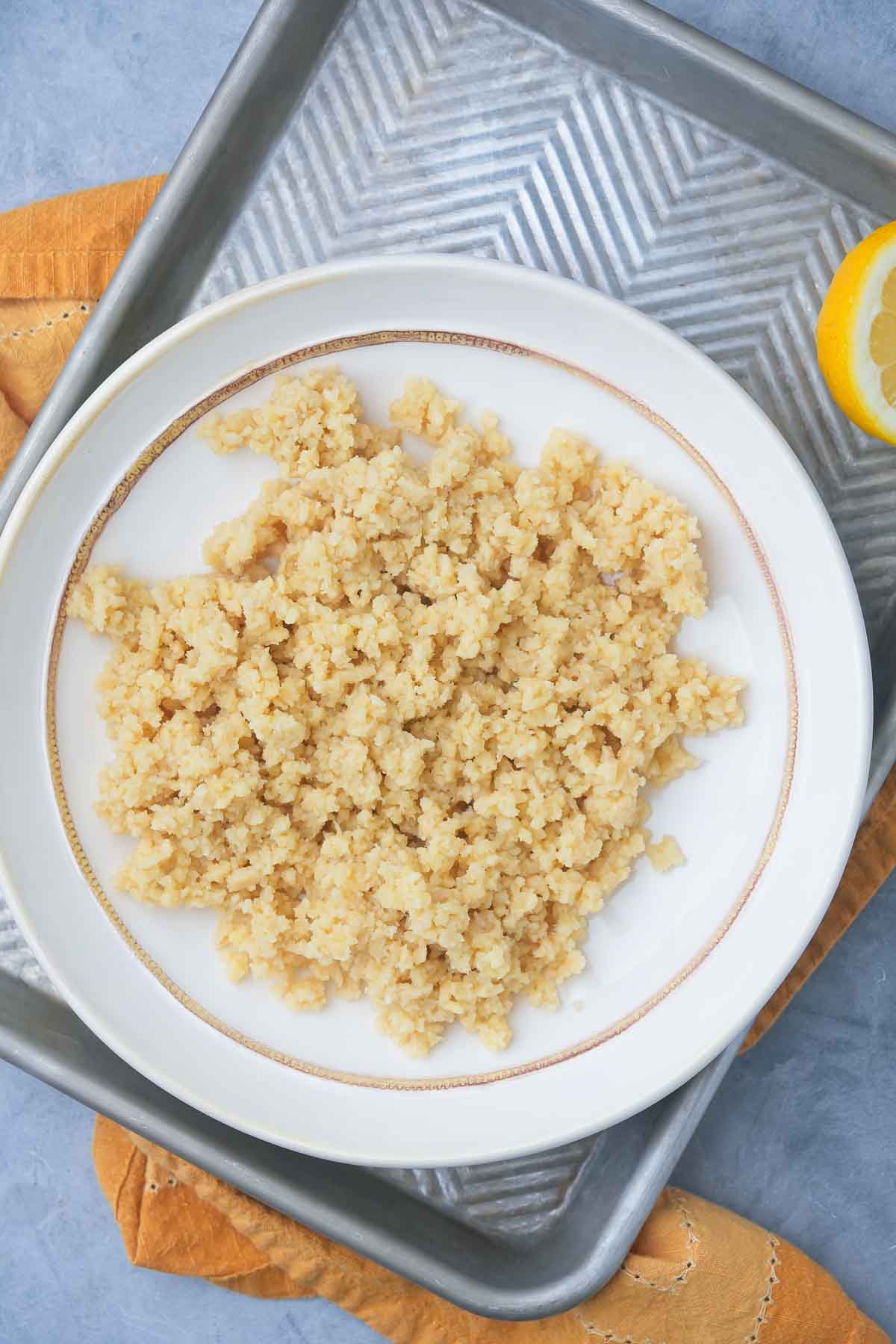 A plate of ground Vegan Cotija Cheese on a metal tray with a yellow napkin and lemon slice in the background.
