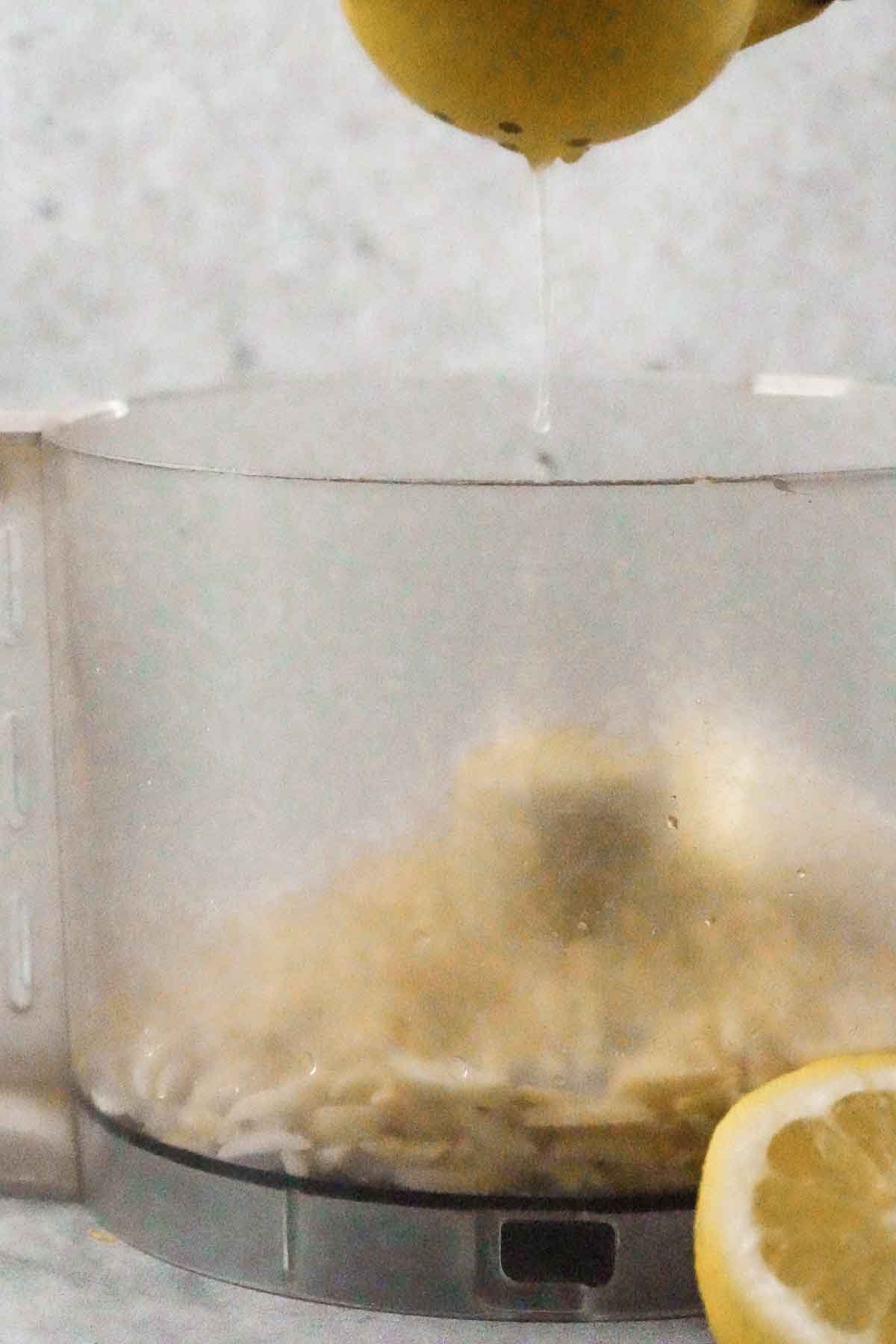 Lemon juice freshly squeezed into a food processor, with a halved lemon visible beside the cup.