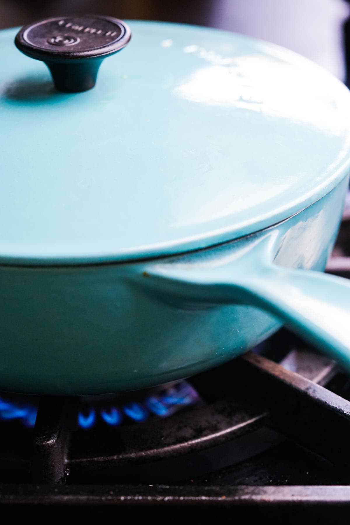 A light blue saucepan with a lid on a gas stove burning with a blue flame.