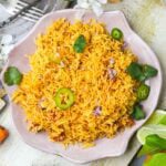 A plate of Vegan Mexican Rice garnished with cilantro and slices of green chili, surrounded by forks and fresh ingredients.