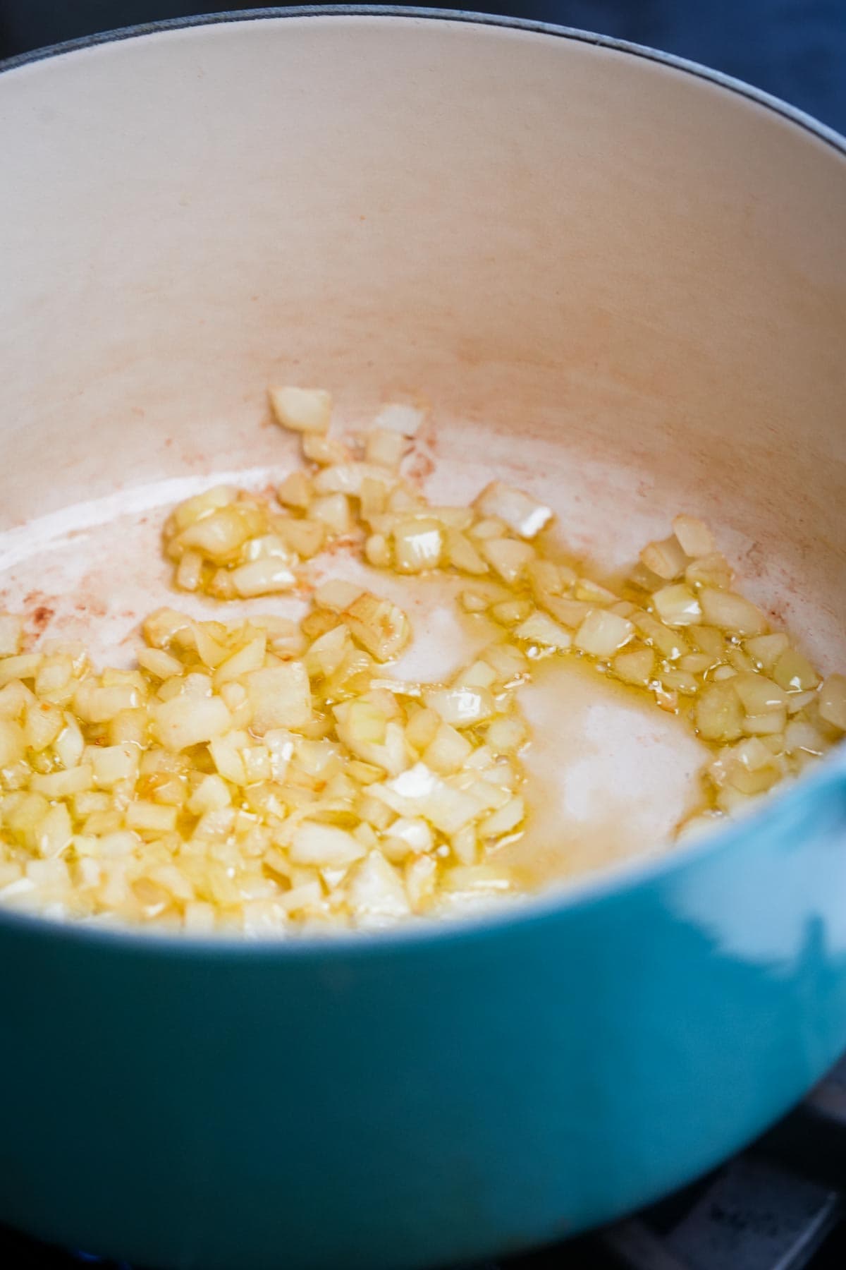Diced onions sautéing in oil in a light blue enamel pot.