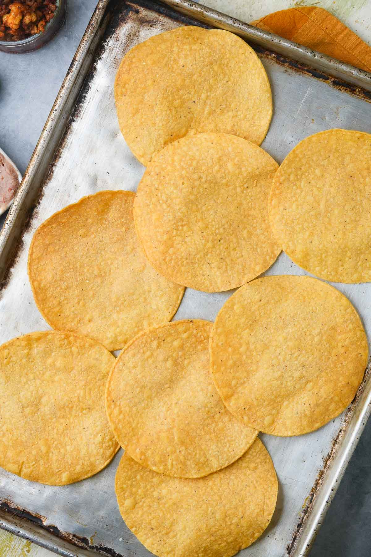 Freshly baked corn tortillas on a metal baking sheet, slightly overlapping, with a rustic background.