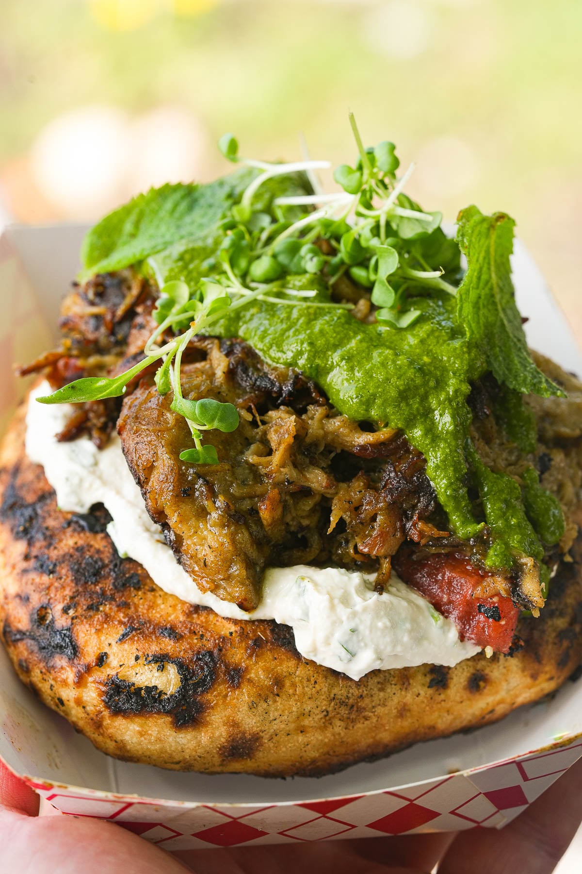 A galactic megastallion grilled sandwich topped with shredded meat, white sauce, green sauce, and fresh greens, served in a cardboard tray.