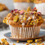 A close-up of a Vegan Pumpkin Muffin topped with chopped nut , rose petals, and icing.