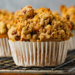 Close-up of a vegan vegan sweet potato muffin with a pecan topping set in a white paper liner, resting on a wire cooling rack.