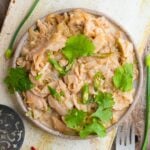 A plate of shredded cooked jackfruit mixed with green chilies and garnished with cilantro. A fork and some green onions are beside the plate.