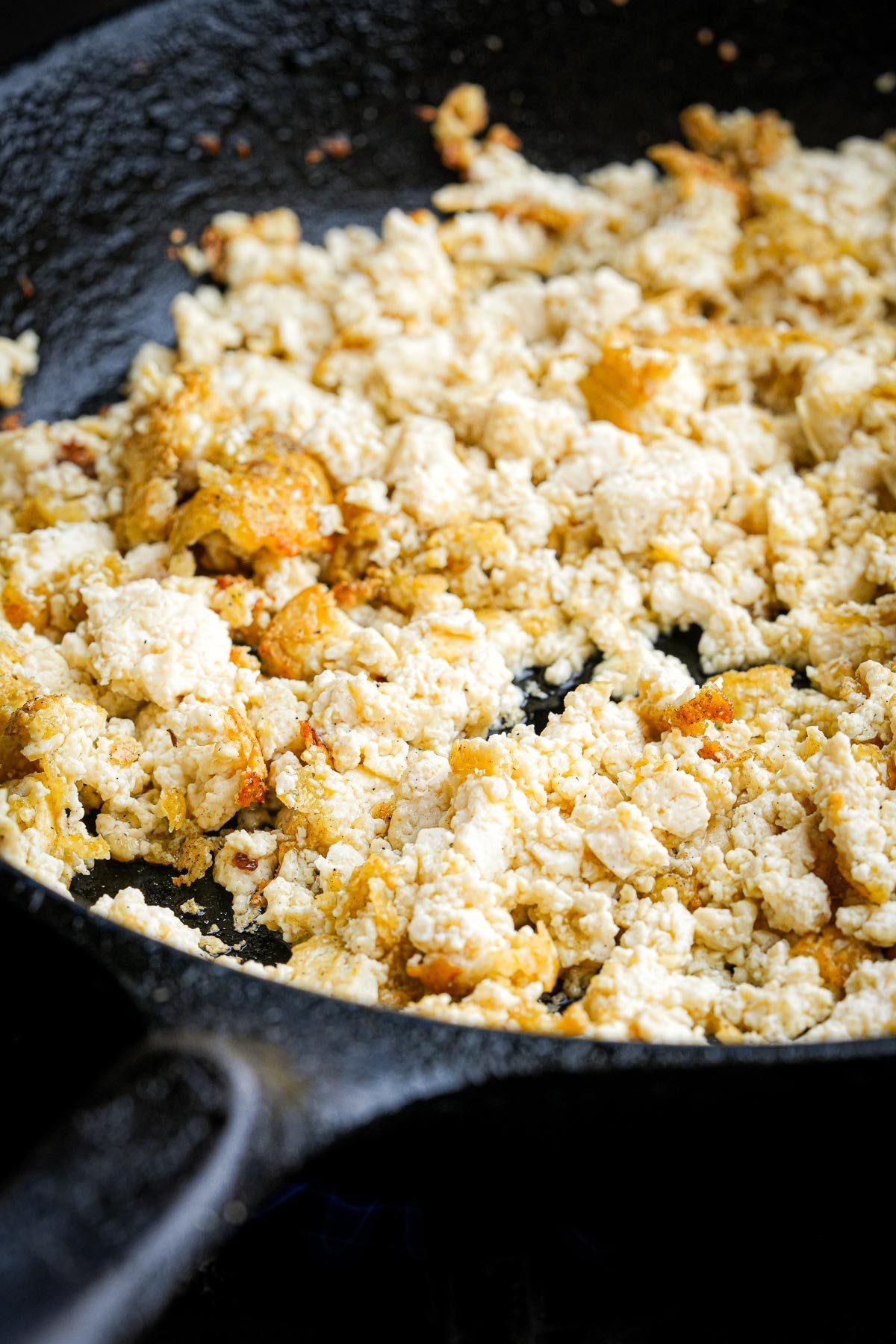 Sautéed crumbled tofu cooking in a black skillet. The tofu is lightly browned.