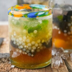 A colorful glass of Sagot Gulaman. Some ice cubes are on the wooden surface nearby.