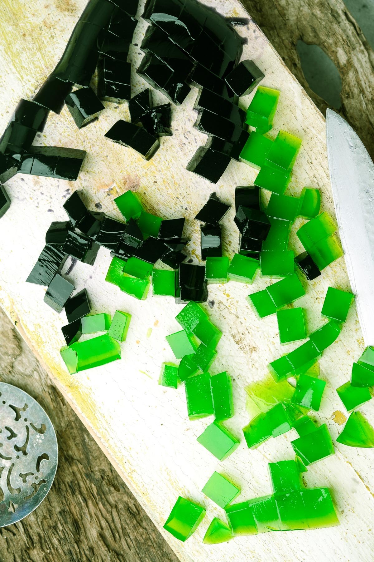 A cutting board with diced green and black vegan pandan jellies for making sago and gulaman.