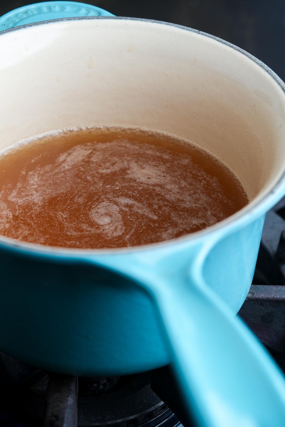 A light blue pot filled with simmering brown liquid on a stovetop.