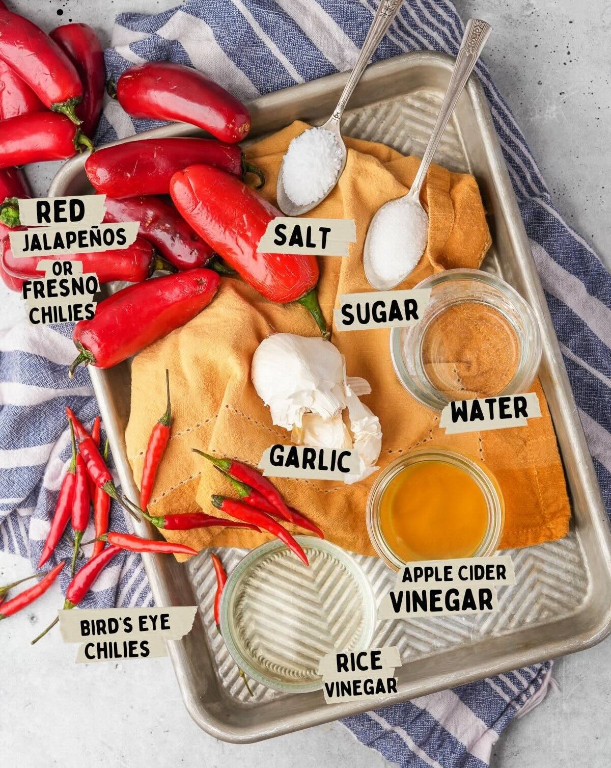 Ingredients for making hot sauce, perfect for a sriracha recipe, displayed on a tray include red jalapeños, bird's eye chilies, garlic, salt, sugar, water, apple cider vinegar, and rice vinegar.
