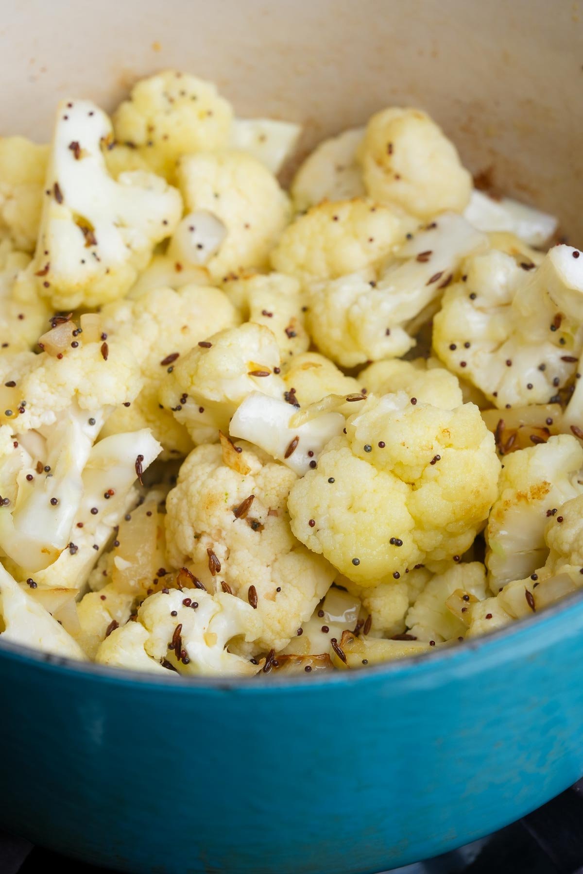 A close-up of cooked cauliflower florets seasoned with seeds, inside a blue pot.