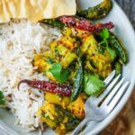 A plate of white rice served with Beerakaya Sabji garnished with cilantro, dried red chilies, and green peppers. A piece of flatbread is placed on top. A fork is on the side of the plate.