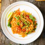A plate of Lao Papaya Salad with vegetables, garnished with peanuts, cilantro, and a lime wedge.